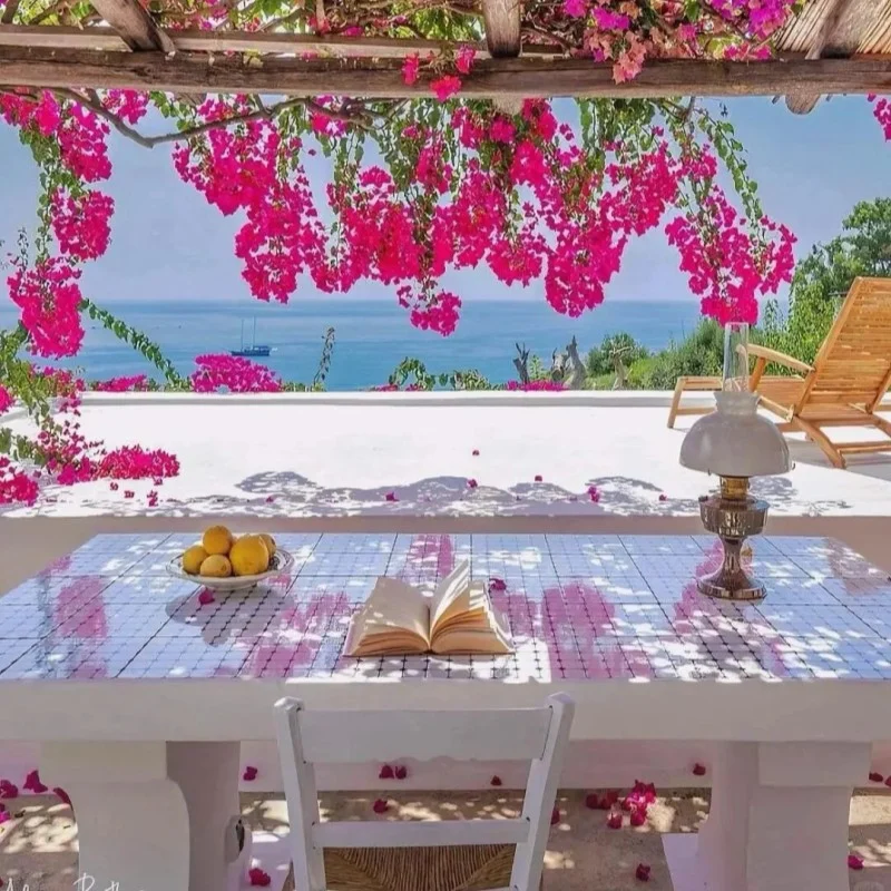 White table with open book and fruit bowl under vibrant pink bougainvillea flowers with sea view terrace