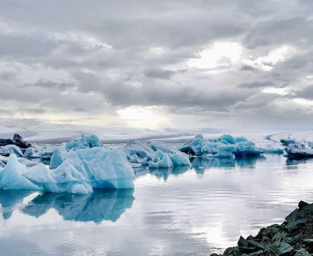 Serene glacier lagoon in Iceland with floating icebergs reflecting in still water under cloudy sky