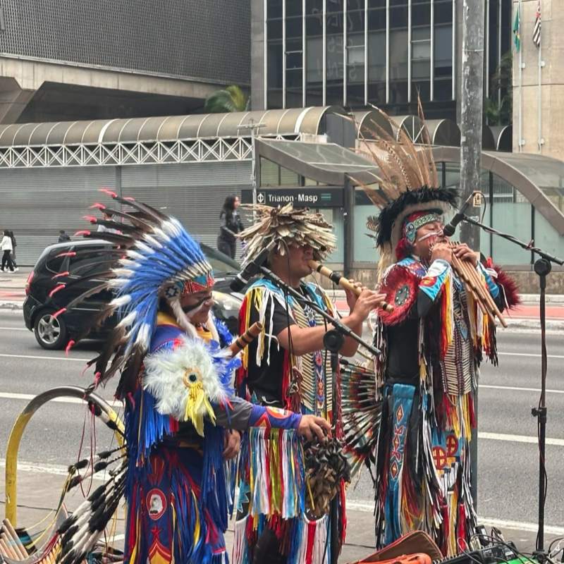 Indigenous performers in traditional feathered headdresses and colorful costumes playing music on city street