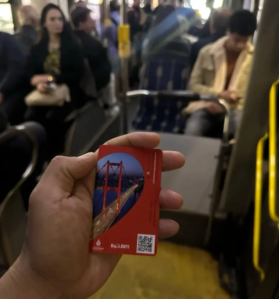 Hand holding red Istanbul transport card inside metro train with passengers