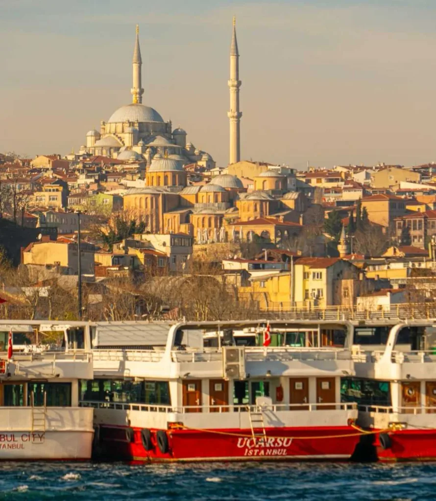 Historic Ottoman mosque overlooking the Bosphorus with traditional ferry boats in foreground during sunset