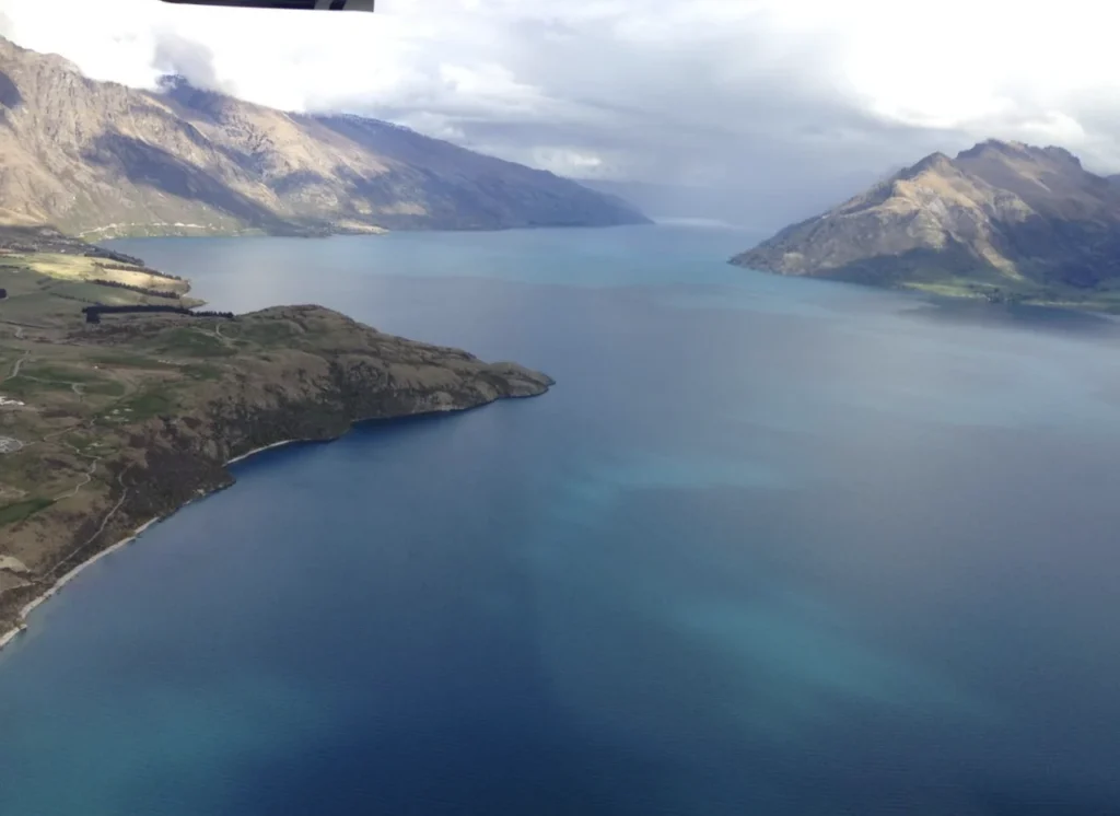 Two yellow kayaks with two people paddling on a large body of water, flanked by steep, dark green mountains on a sunny day in a fjord.