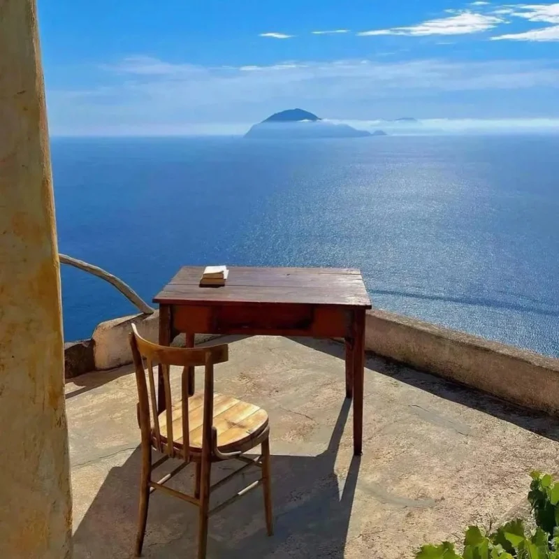 Simple wooden desk and chair overlooking the deep blue Mediterranean Sea with distant island on the horizon