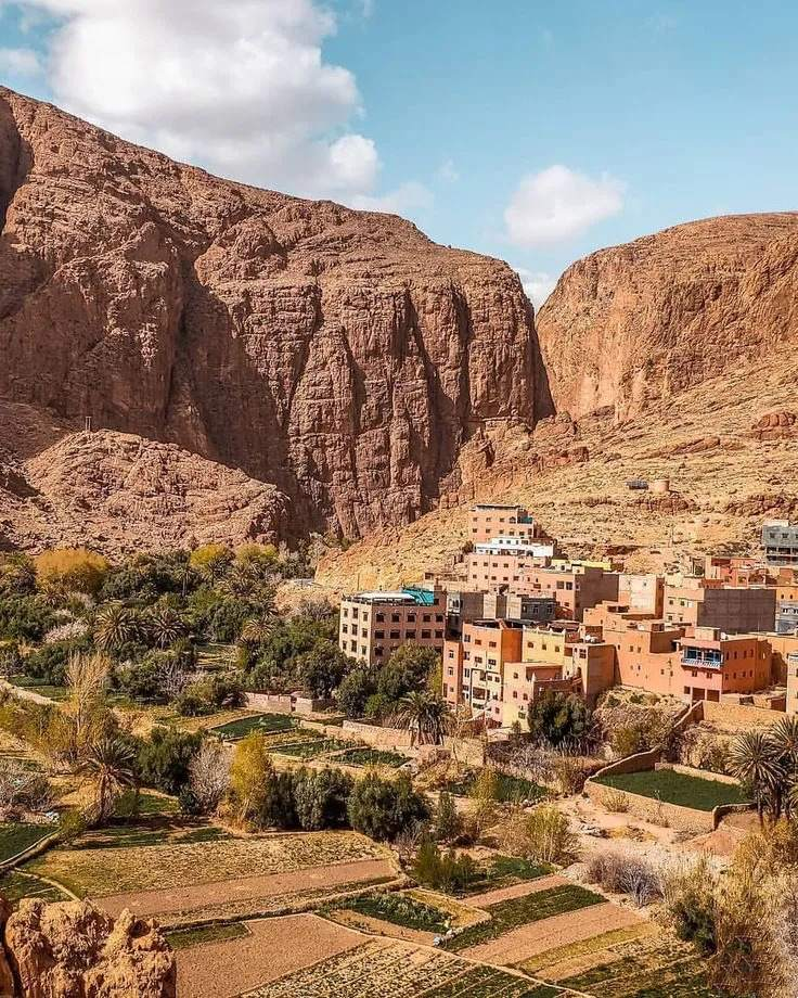 Traditional Moroccan village nestled in dramatic red rock canyon with terraced gardens and mud brick buildings