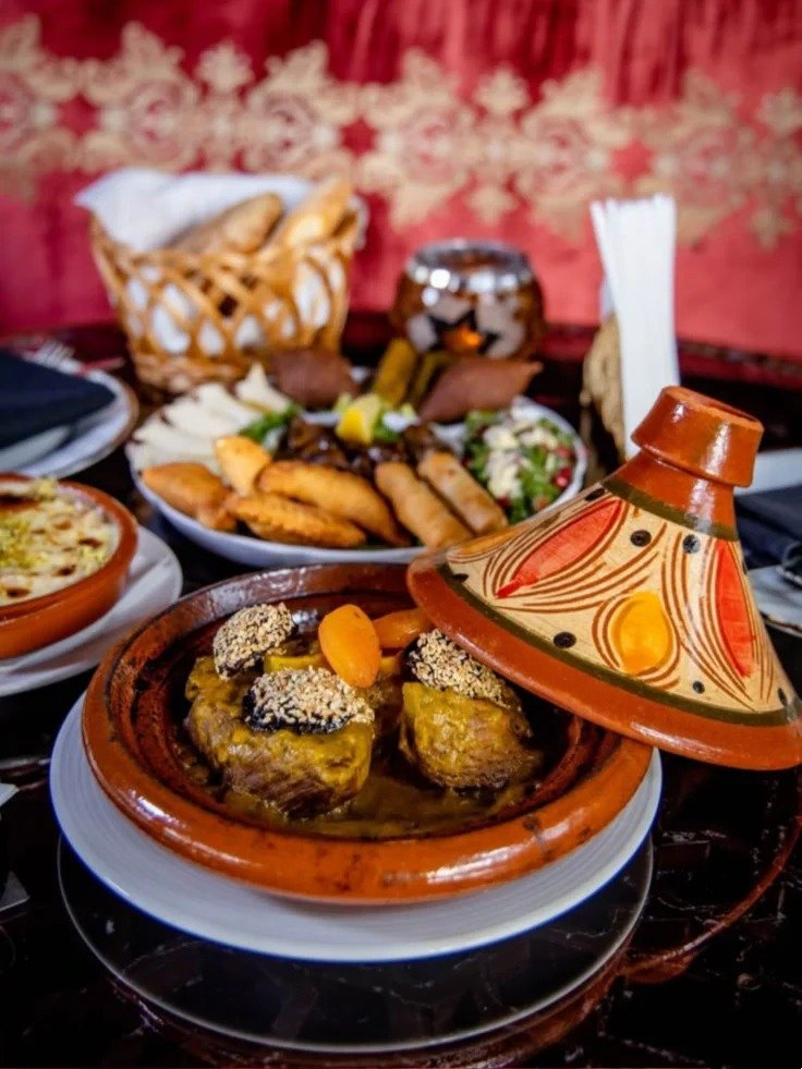 Traditional Moroccan tagine pot with slow-cooked meat and vegetables alongside authentic bread and accompaniments
