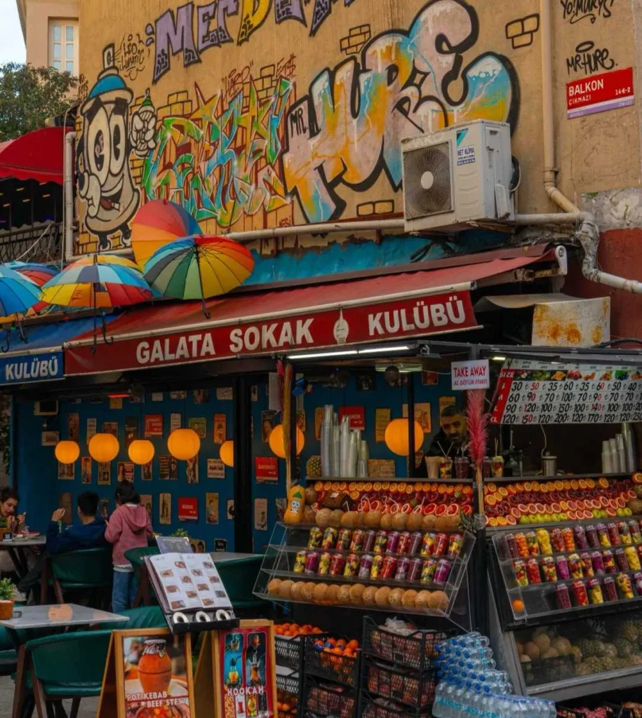 Local Turkish street vendor selling fresh fruits beneath vibrant graffiti wall art in urban setting
