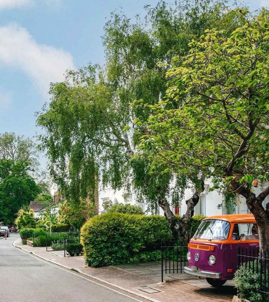 Colorful vintage Volkswagen bus parked on peaceful European street with green trees and white buildings