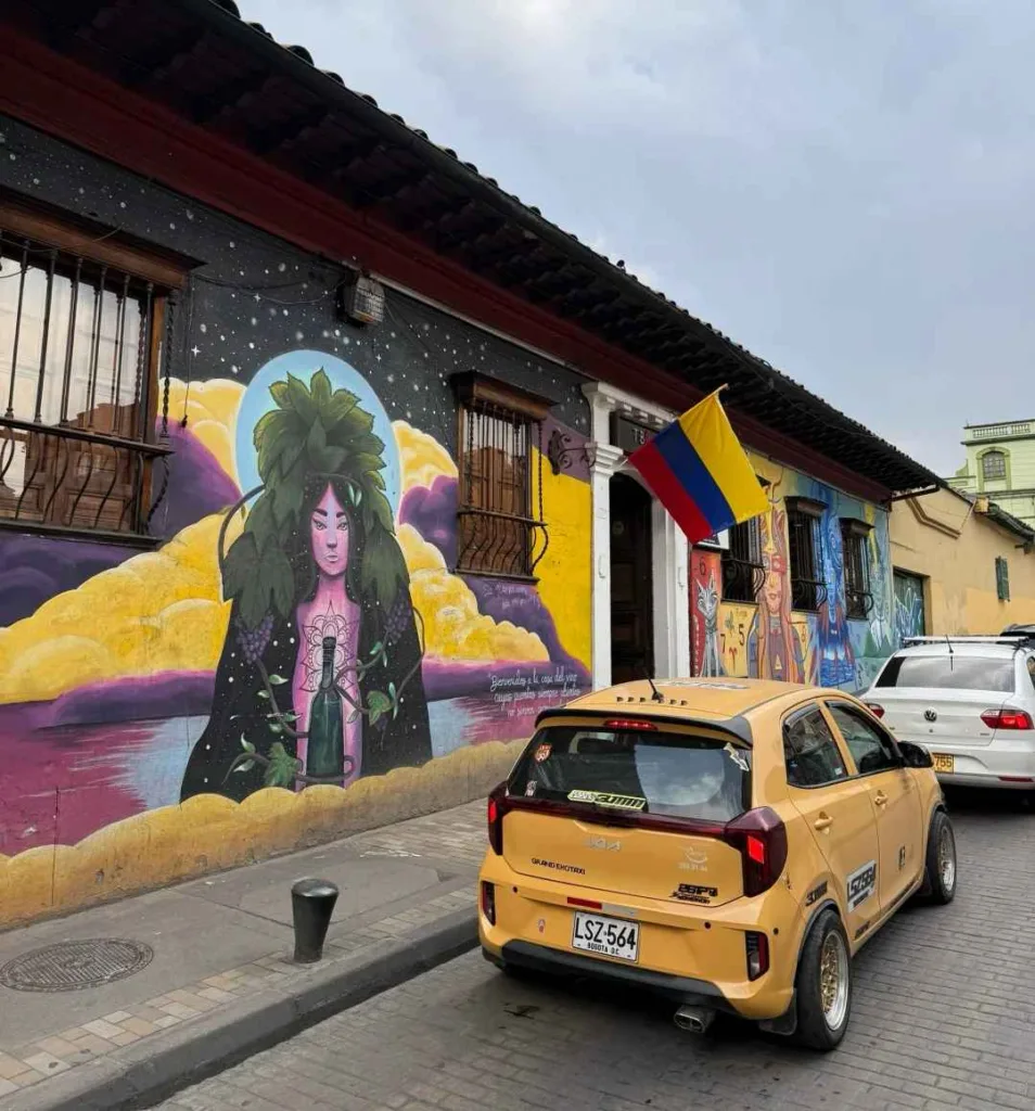 Colorful street art mural featuring woman with Colombian flag and yellow taxi in Bogotá La Candelaria district