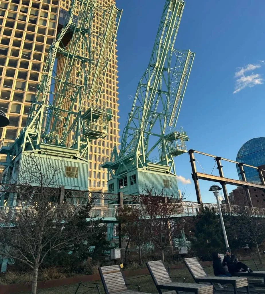 Brooklyn Bridge Park with modern seating overlooking Manhattan skyline and construction cranes in DUMBO neighborhood