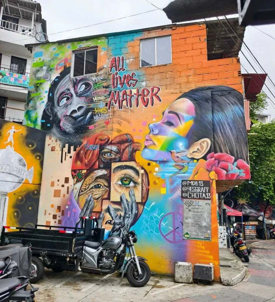 Large colorful street art mural featuring portraits and "All Lives Matter" text on building wall in Colombian urban area