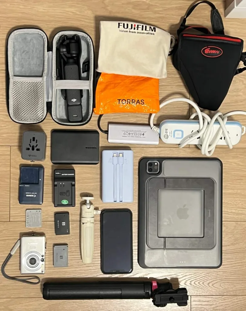 Organized flatlay of essential solo travel gear including DJI drone, power banks, universal adapter, cables, camera equipment and protective cases