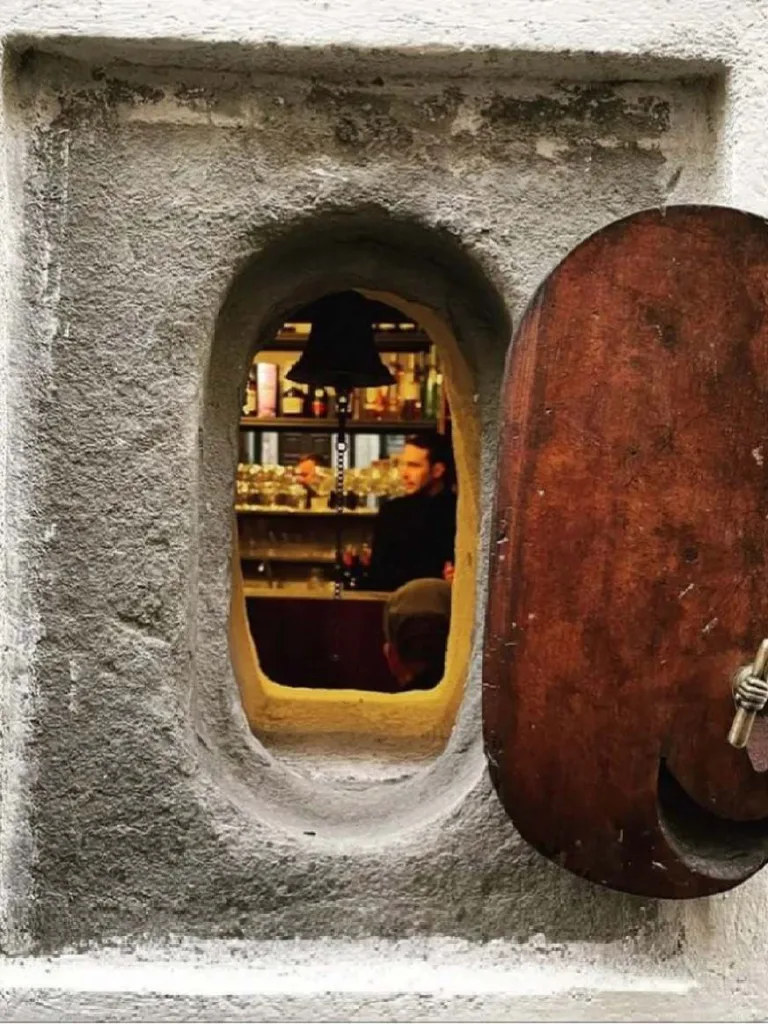 Open wine window revealing glimpse into Florence wine shop interior with wooden door and stone archway