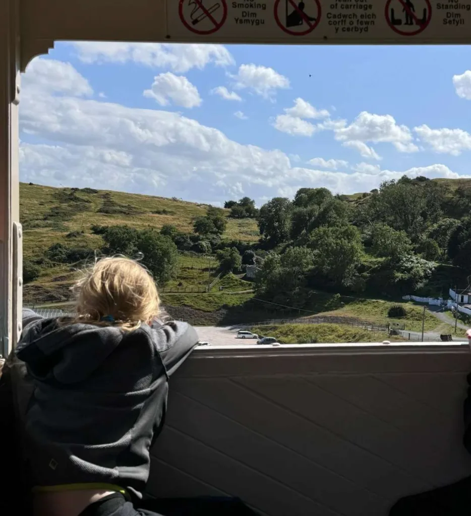 Passenger enjoying panoramic mountain and countryside views from inside Great Orme Tramway carriage in Llandudno