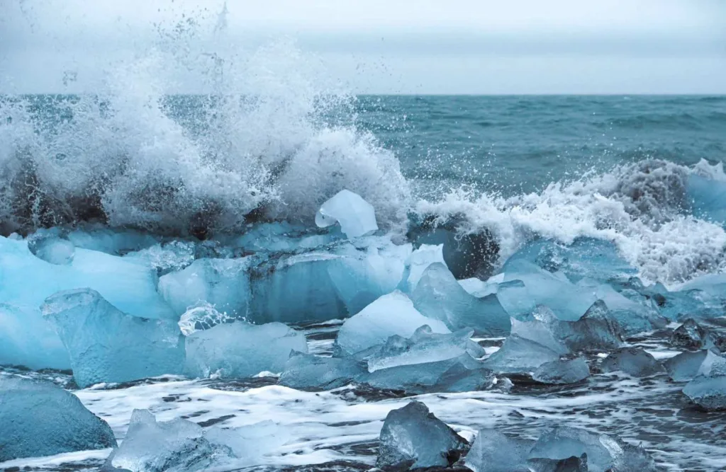Crystal clear icebergs washed up on black volcanic beach with ocean waves crashing in Iceland