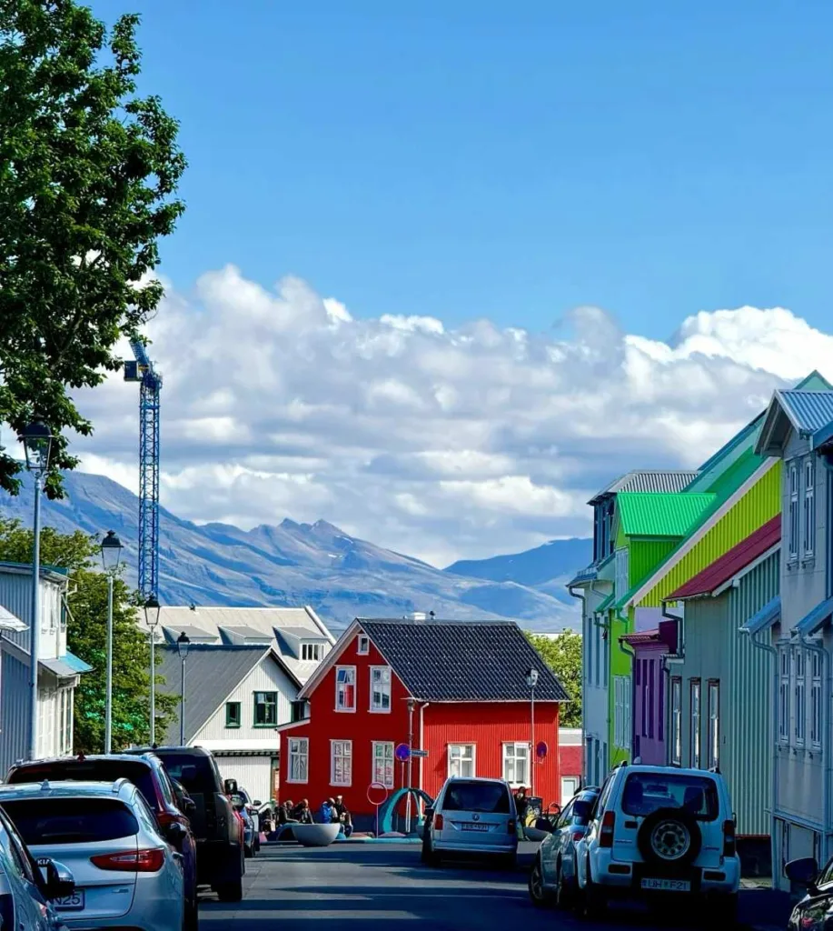Vibrant colorful houses lining Reykjavik street with snow-capped mountains in background and parked cars