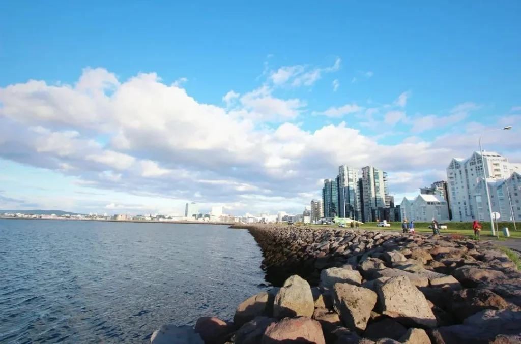Reykjavik waterfront promenade with rocky coastline, modern buildings and people walking along scenic path