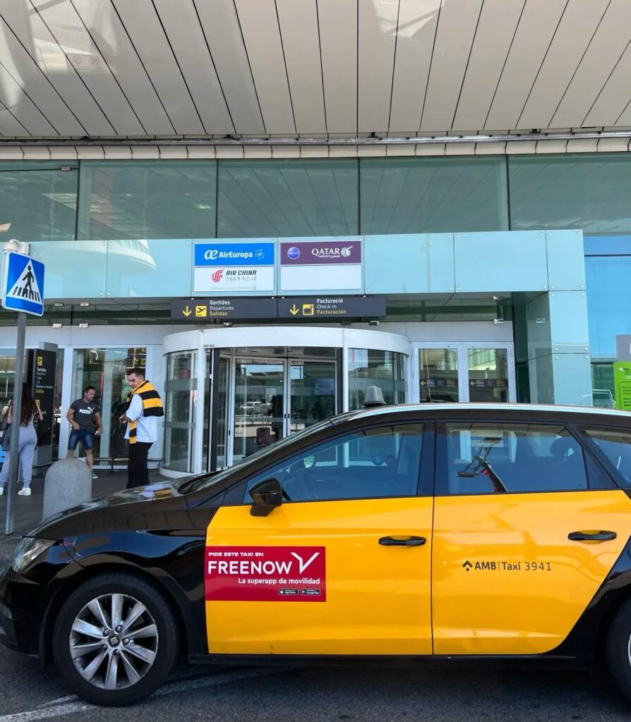 Official Barcelona airport taxi with FreeNow app branding waiting outside terminal building for passenger pickup