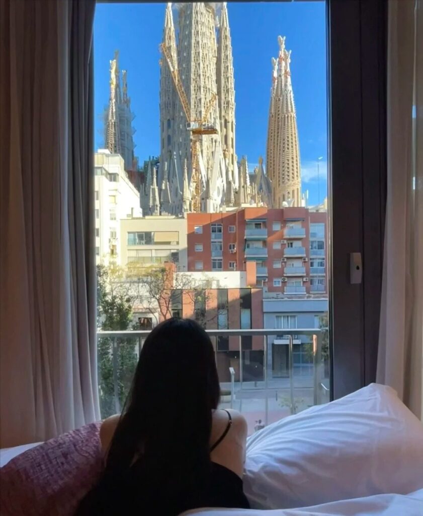 Stunning hotel room view of Barcelona's Sagrada Familia cathedral from comfortable accommodation bed with large windows