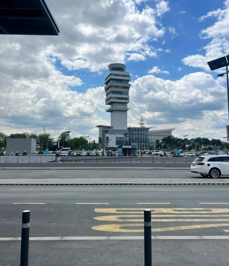 Modern Belgrade airport terminal building with distinctive control tower under dramatic cloudy sky, showing airport's contemporary infrastructure