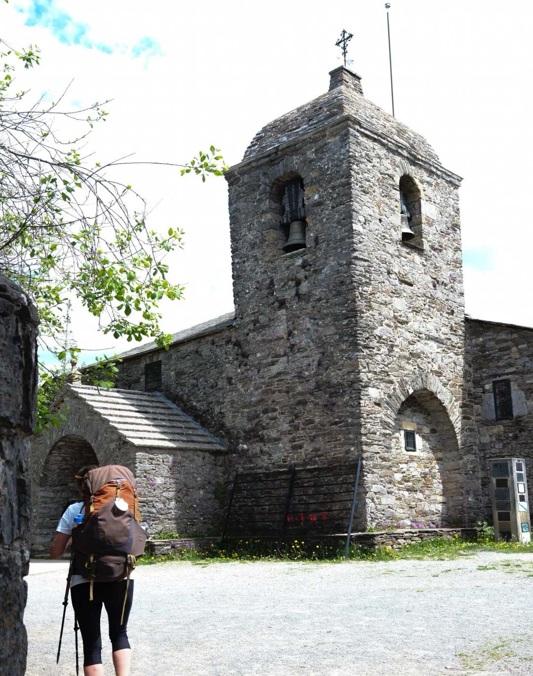 First Camino pilgrim with backpack visiting historic stone church with bell tower along the route