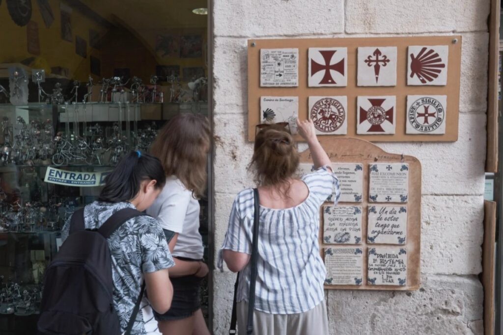 First-time Camino pilgrims learning about traditional symbols and crosses in Santiago souvenir shop