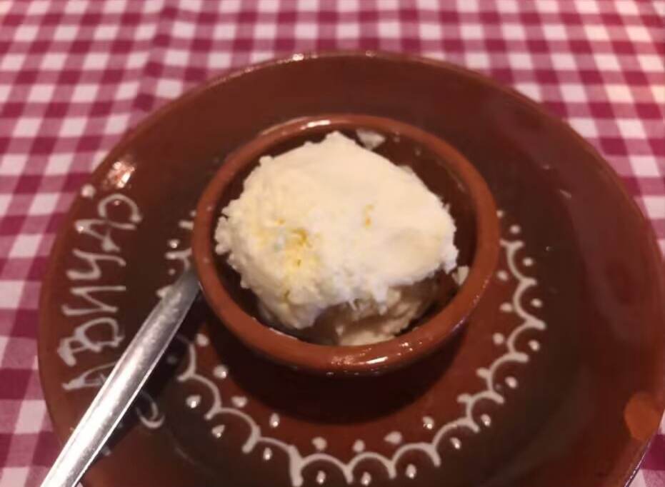 Traditional Serbian kajmak served in clay bowl, creamy white dairy product with rich texture on checkered tablecloth