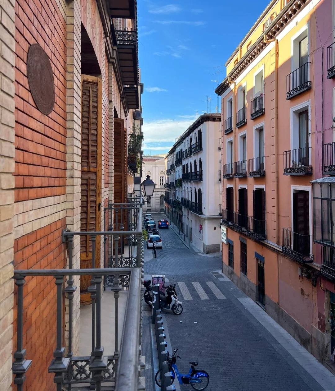 Madrid hotel balcony overlooking narrow historic street with colorful Spanish buildings and iron railings