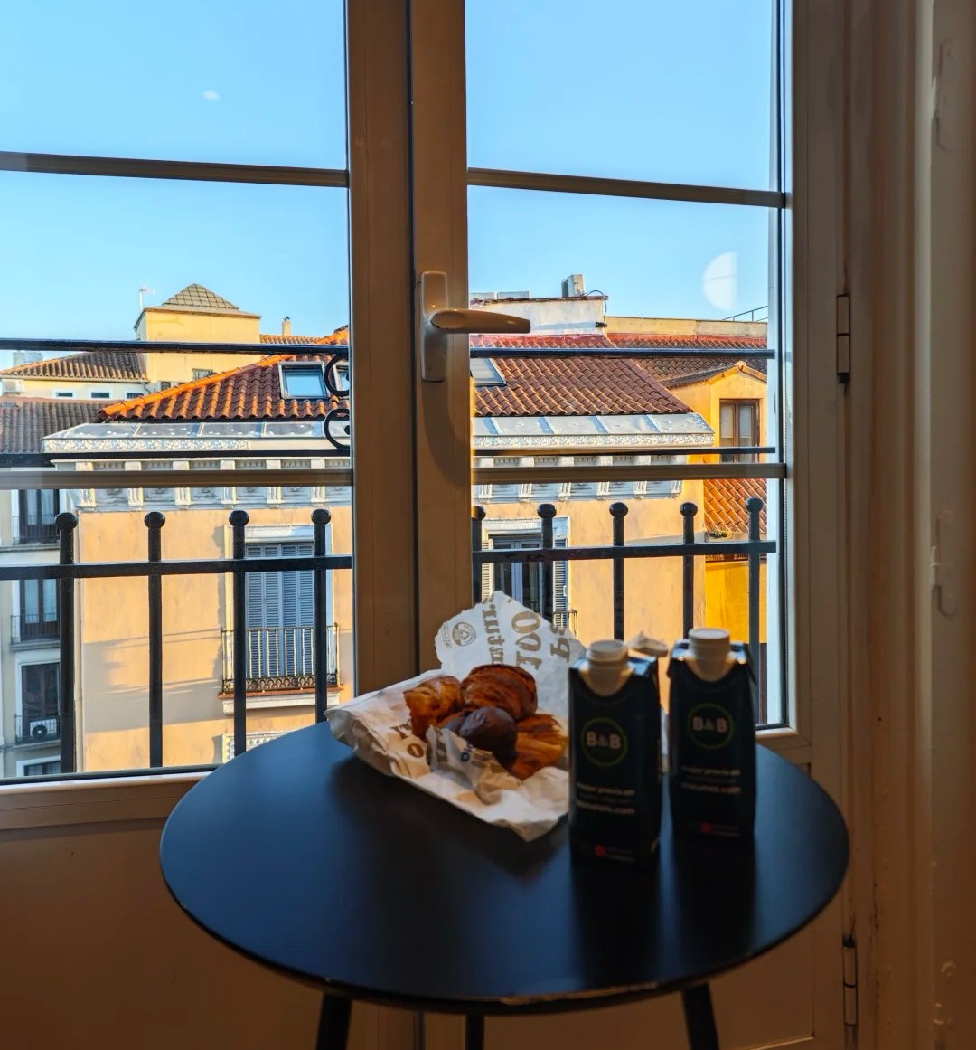 Madrid hotel room with breakfast setup and window view of traditional Spanish rooftops and balconies
