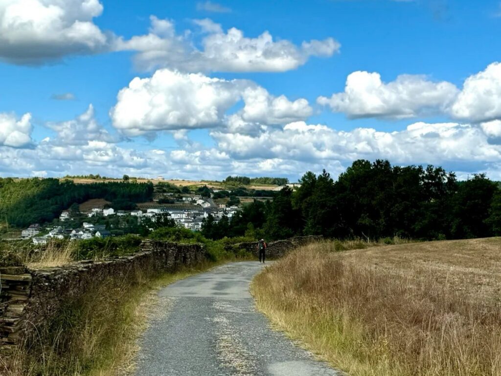 Pilgrim walking on Santiago Ways path approaching Spanish village