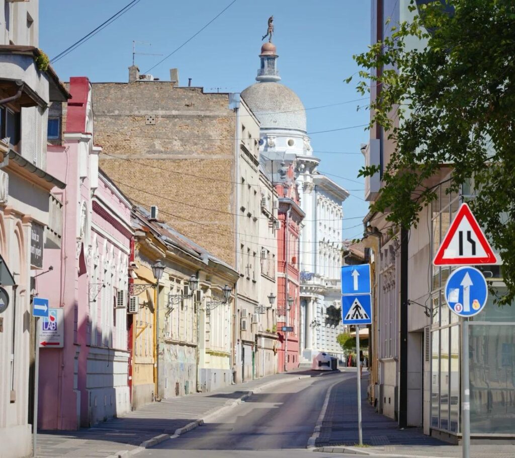 Colorful small town street in Serbia with traditional buildings leading to Orthodox church dome, showing typical provincial urban landscape