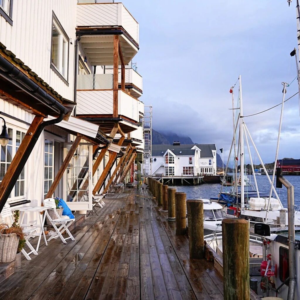 Norway stays unique waterfront cabins on stilts overlooking marina with boats and dramatic mountain backdrop