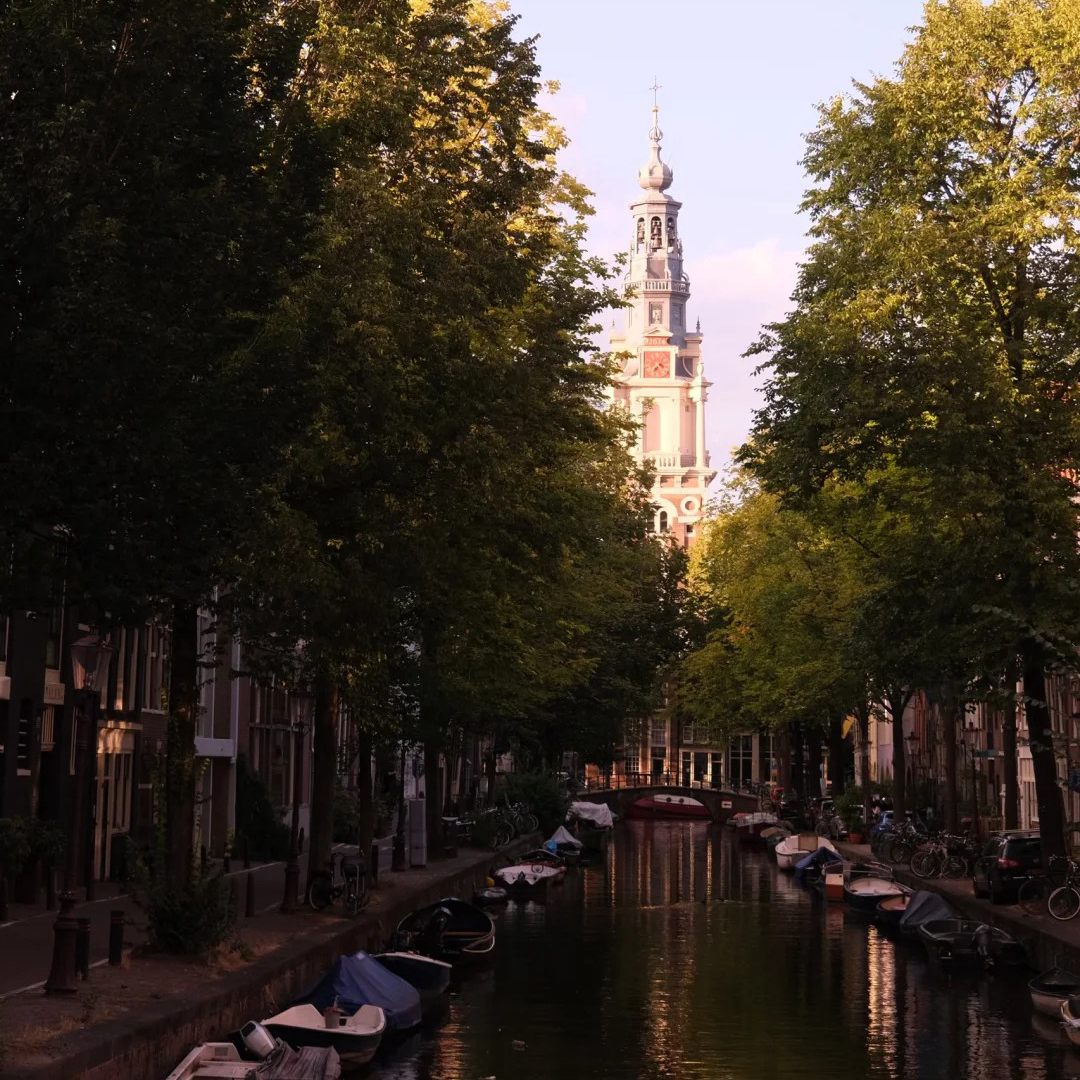 Places stay Amsterdam canal with boats and Zuiderkerk tower in background during golden hour