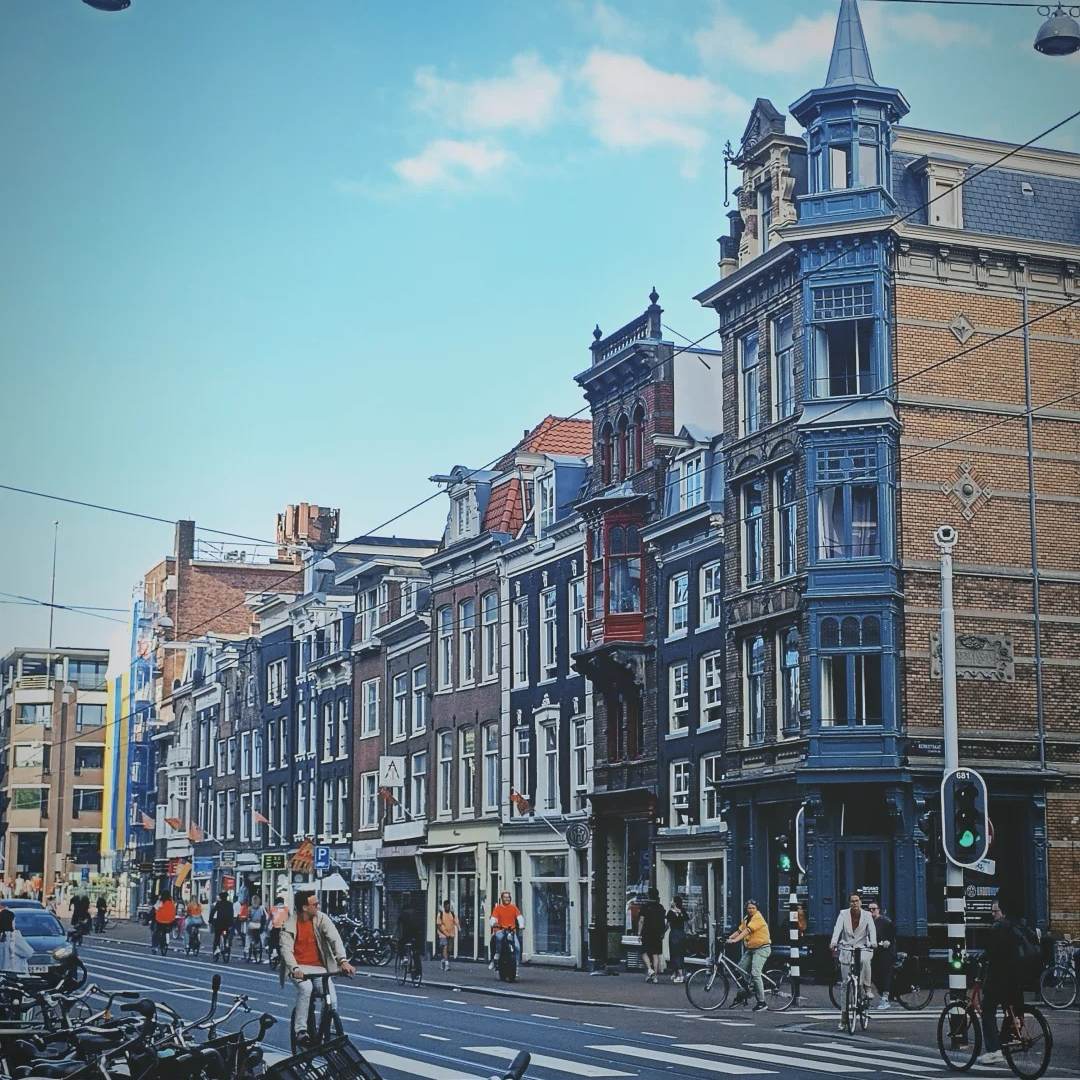 People cycling on a street in downtown Amsterdam, with classic Dutch architecture in the background.
