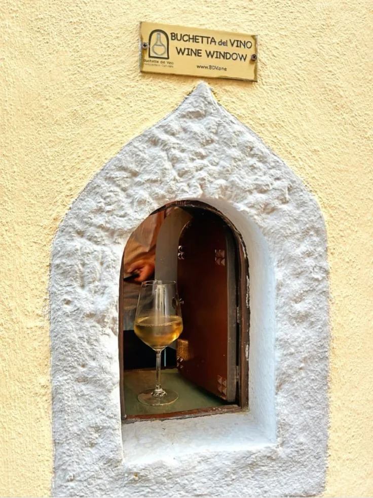 Traditional Italian wine window (buchetta del vino) in stone wall with white wine glass displayed inside