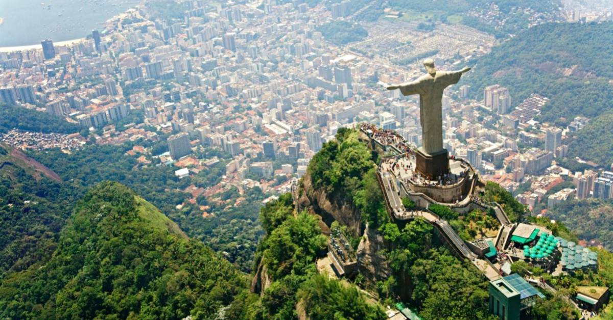 Aerial view of Christ the Redeemer statue overlooking Rio de Janeiro cityscape with mountains and urban sprawl