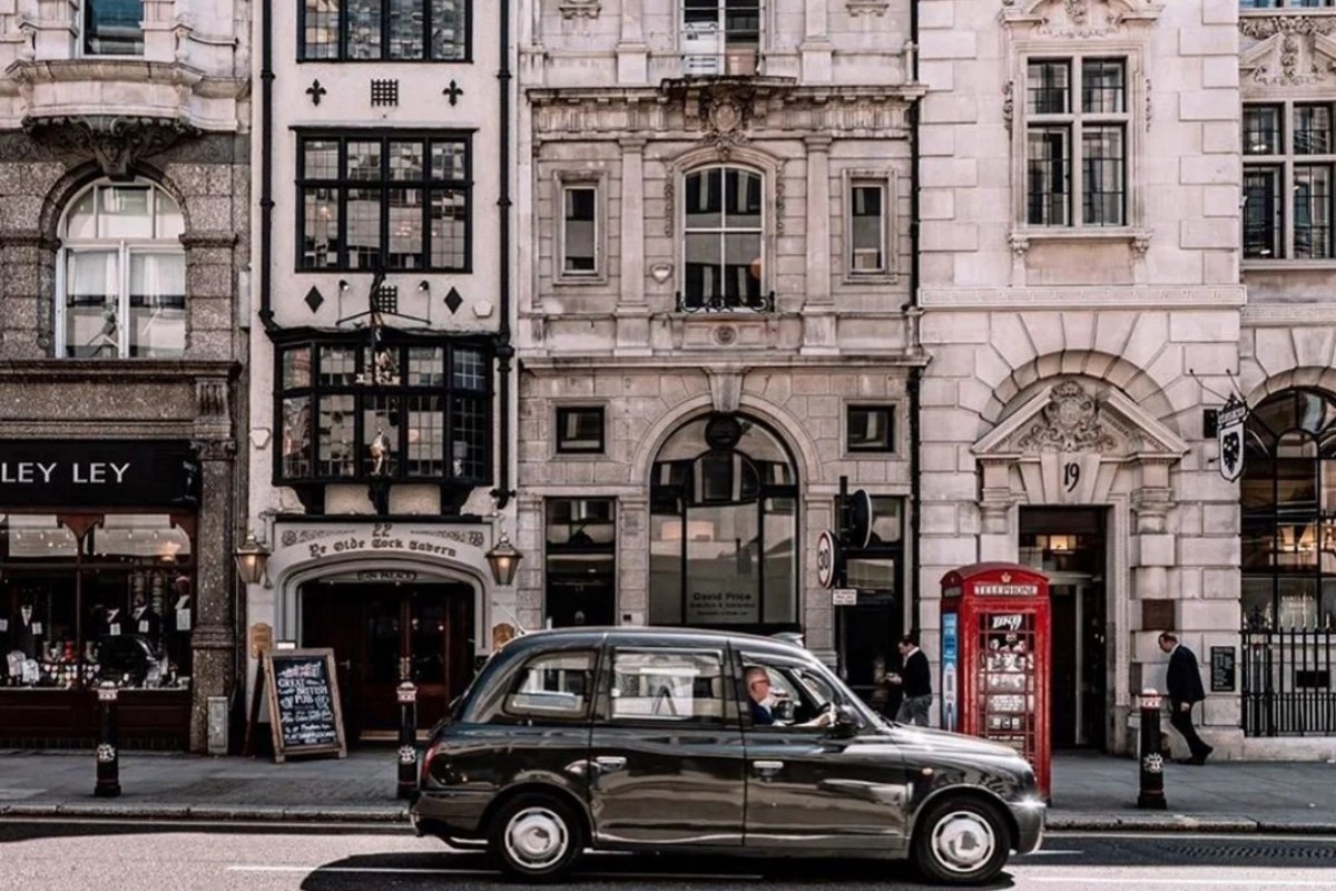 Traditional London black taxi on historic cobblestone street with Georgian architecture and iconic red phone box
