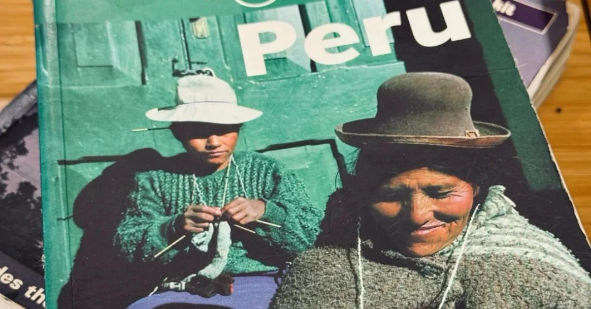 A close-up of a green travel guidebook titled "Peru" on its cover, featuring an image of two individuals wearing traditional hats, with one knitting.