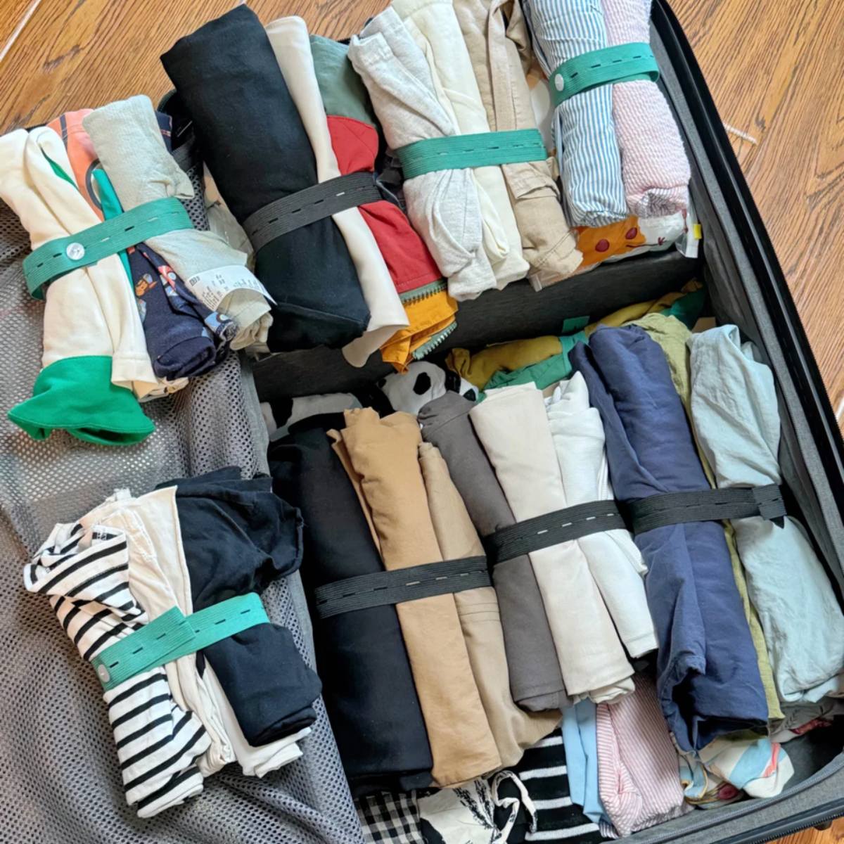 Overhead view of an open suitcase filled with various rolled-up garments, neatly organized and held together with elastic packing bands to maximize space.