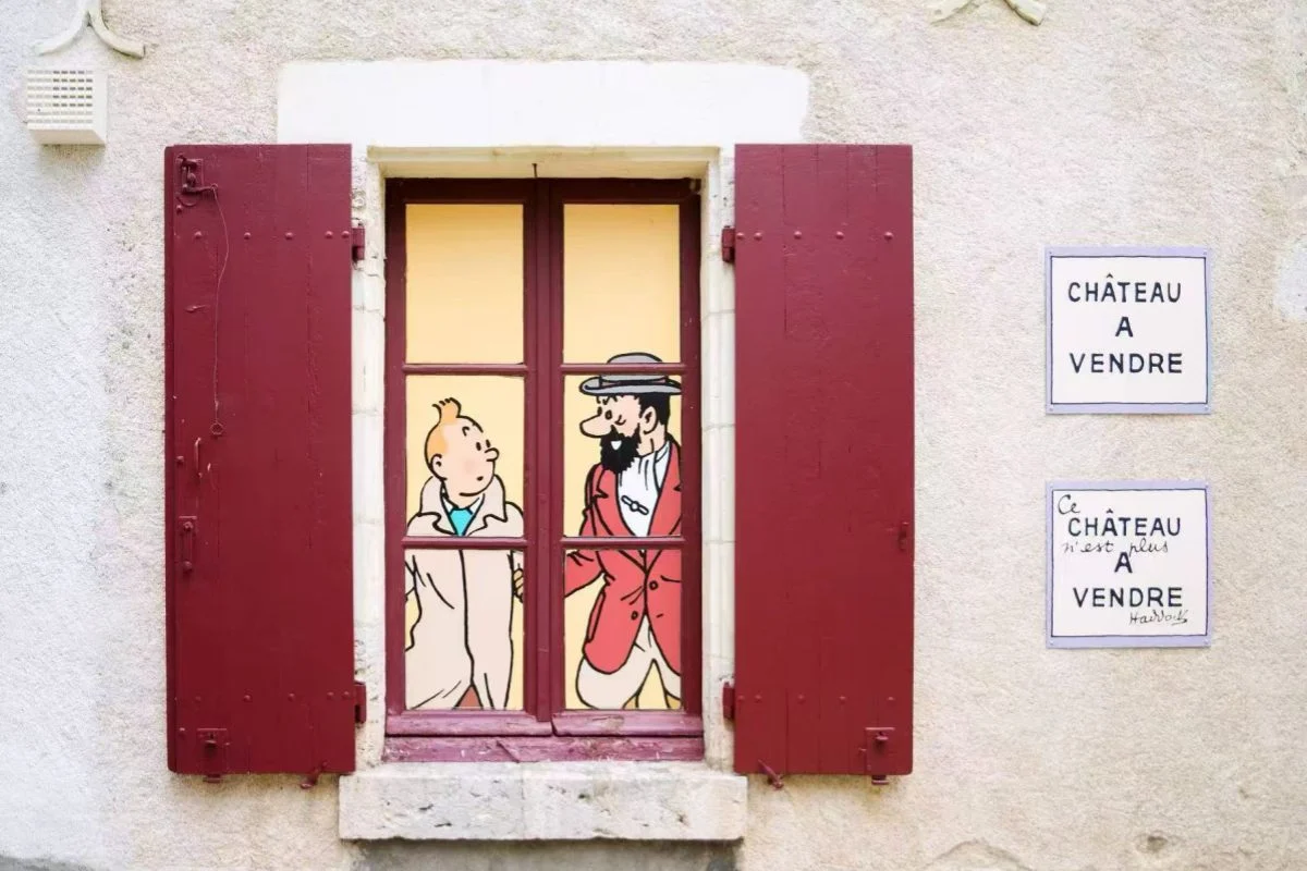 Window with Tintin and Captain Haddock comic characters painted on glass with red shutters and 'Chateau a Vendre' signs
