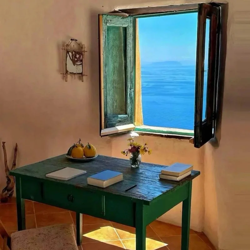 Rustic green wooden desk with books by weathered window shutters framing perfect blue Mediterranean sea view