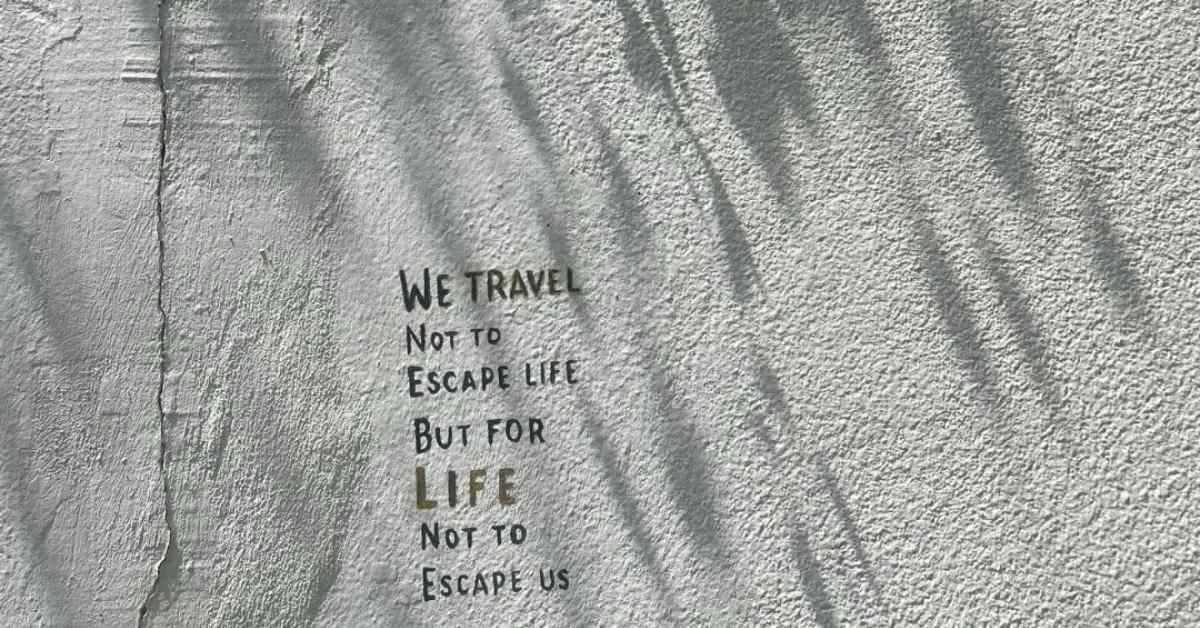 Wall text reading 'We travel not to escape life but for life not to escape us' on concrete with shadows