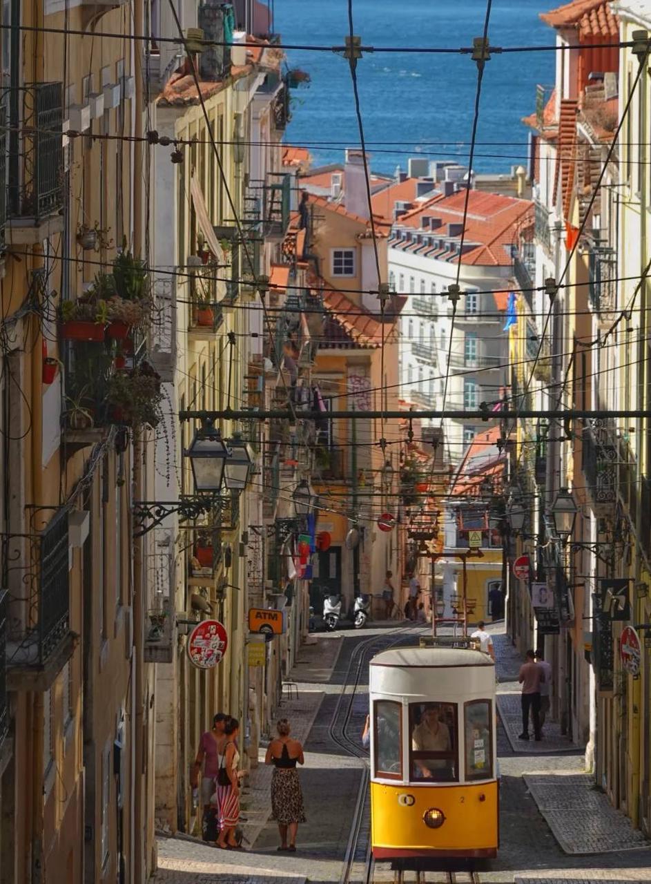 Iconic yellow tram descending a steep street in Lisbon with a stunning blue sea view in the background – Portugal solo travel photography