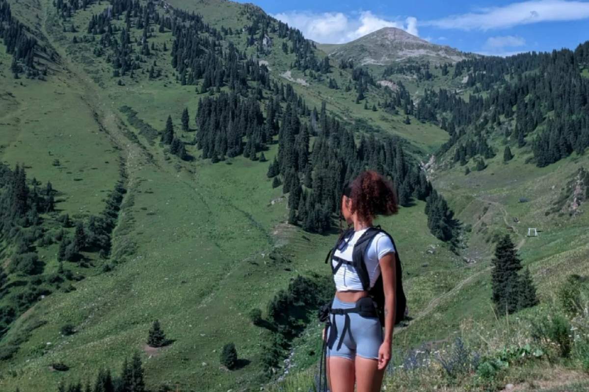 Solo female traveler with backpack overlooking green mountain valley and alpine peaks during hiking adventure