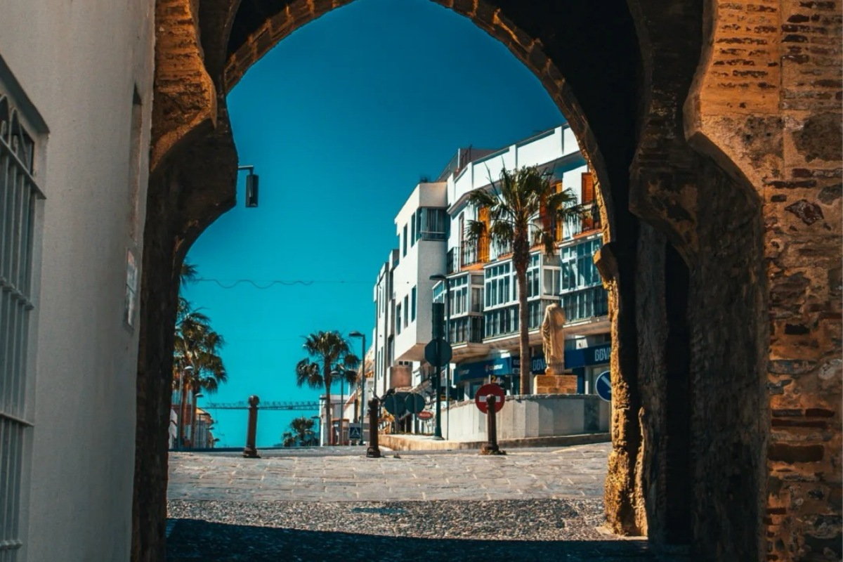 Ancient stone archway in Barcelona's Gothic Quarter framing colorful buildings and palm trees with blue Mediterranean sky