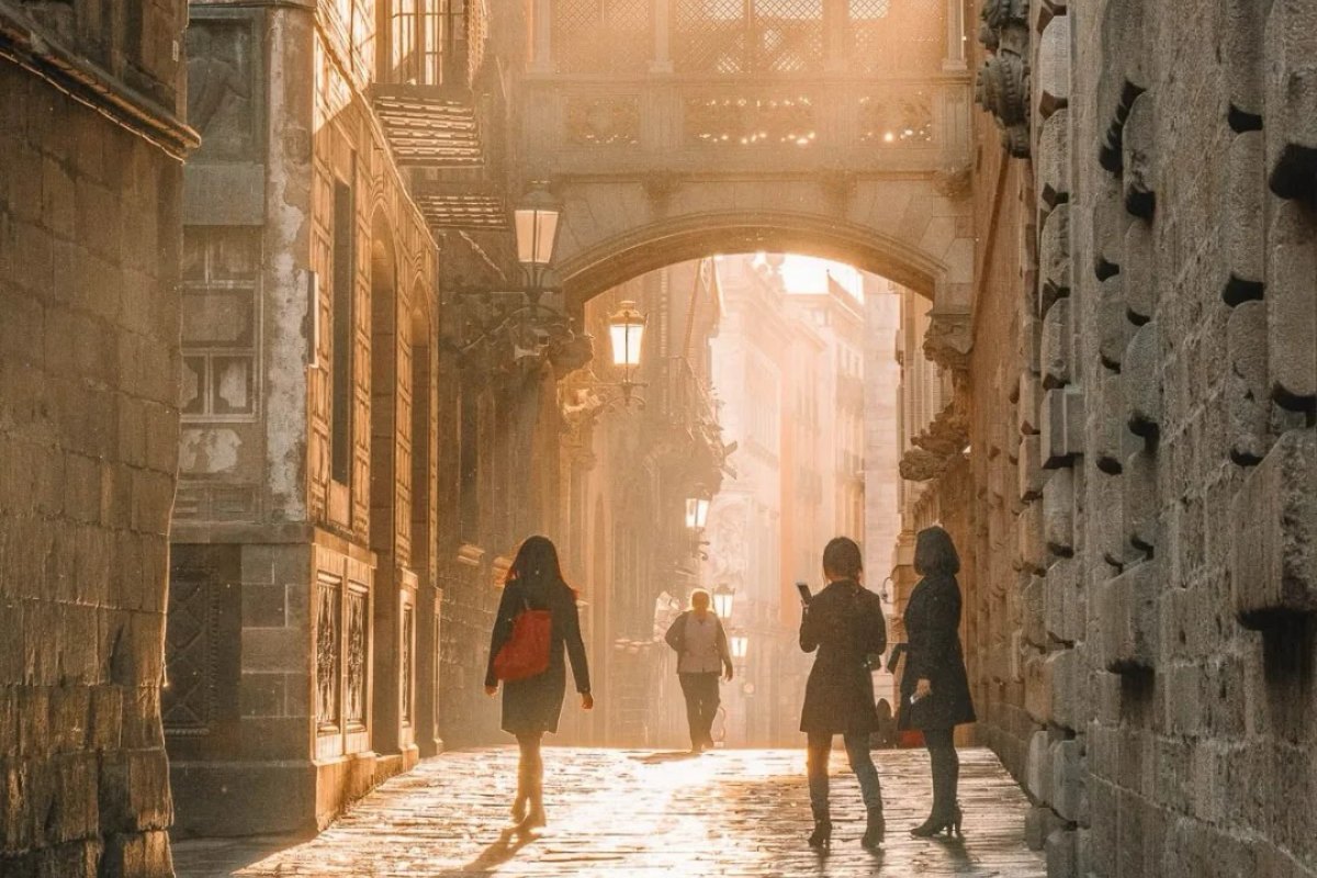 Historic Gothic Quarter street in Barcelona with stone bridge connecting medieval buildings in warm golden sunlight