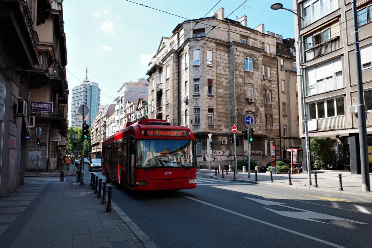 Red Belgrade city bus number 2012 traveling through historic downtown street with mix of old Austrian-Hungarian and modern architecture