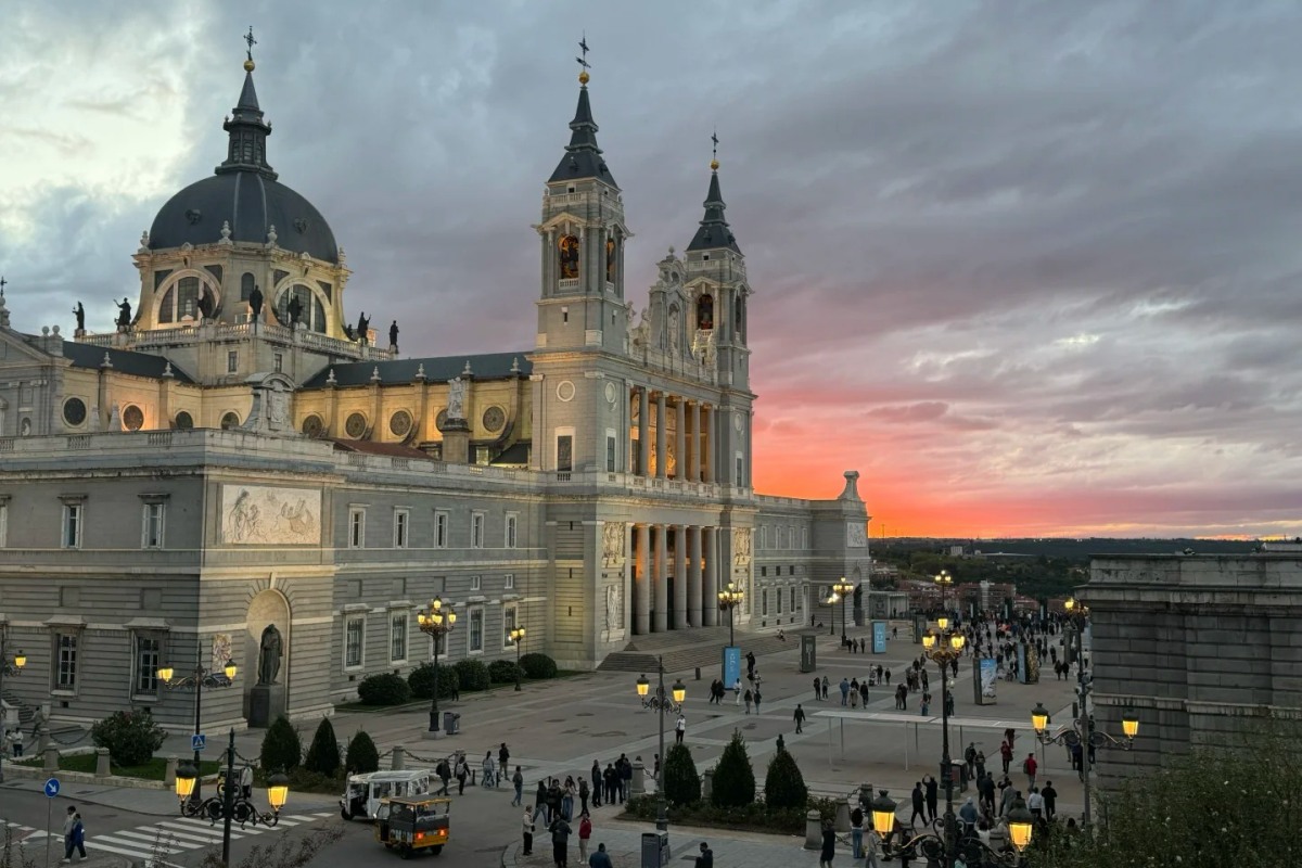 Stunning sunset view of Madrid's Almudena Cathedral and Royal Palace complex with dramatic evening lighting and visitors