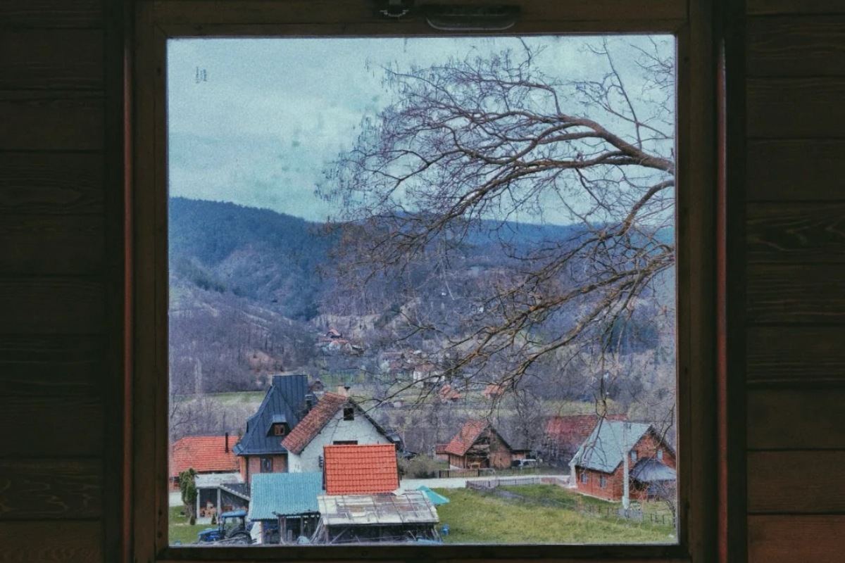 View through traditional house window showing Serbian mountain village with red tile roofs nestled in Zlatibor region hills