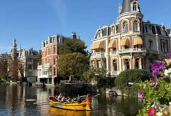 Amsterdam historic canal mansions with yellow kayak and flower-decorated bridge for female travels