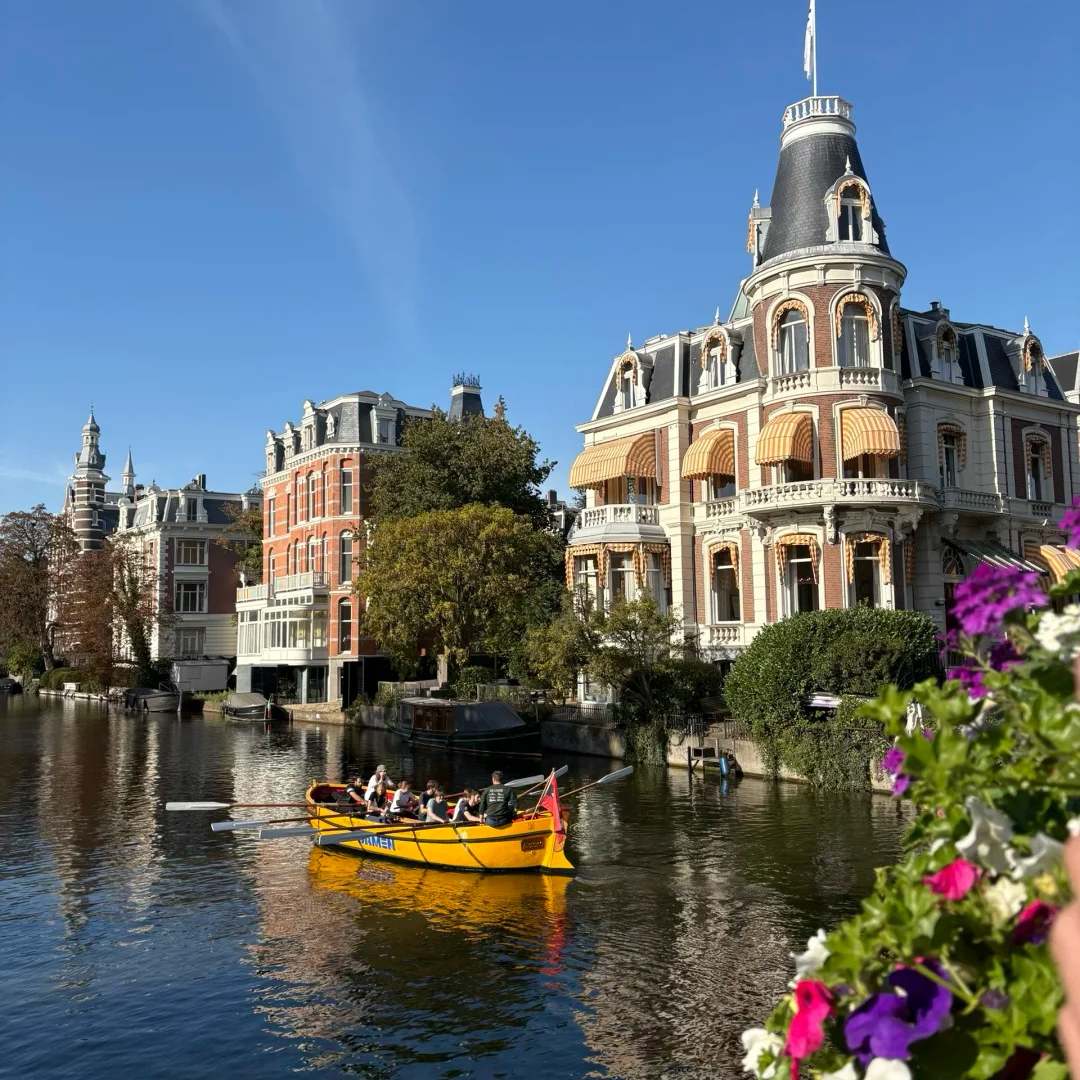 Amsterdam historic canal mansions with yellow kayak and flower-decorated bridge for female travels